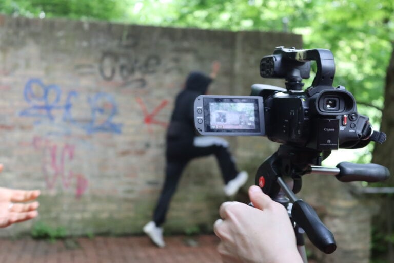 Jugendliche filmen eine actionreiche Szene vor einer Graffitti-Wand.
